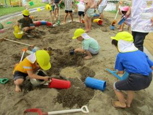 砂場に穴を掘って水を入れる子供たち